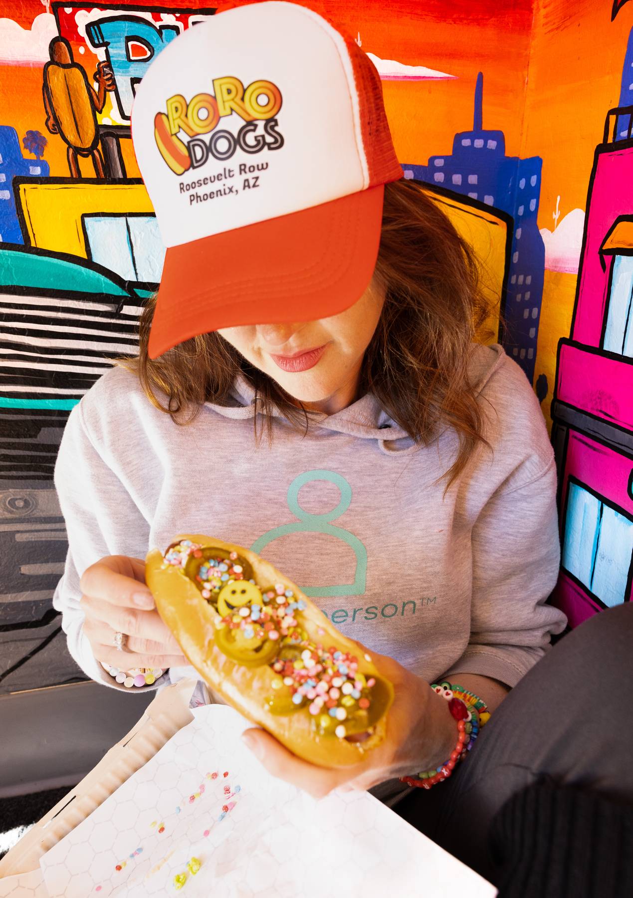 Amanda Renfrew of TheTaxPerson® in a RoRo Dogs hat holding a sprinkle-topped hot dog at a one·n·ten fundraiser
